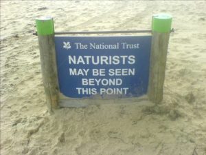 sign in the sand, with text reading, "the national trust
naturists may be seen beyond this point"