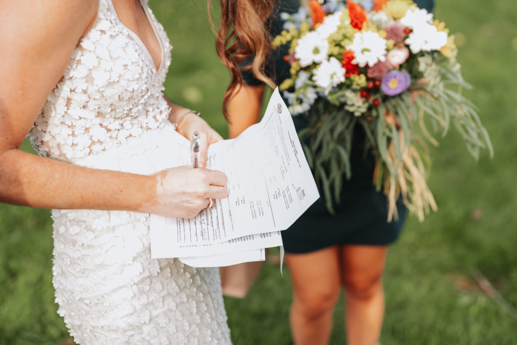 white-clad bride, pictured from the neck down, signing a wedding license